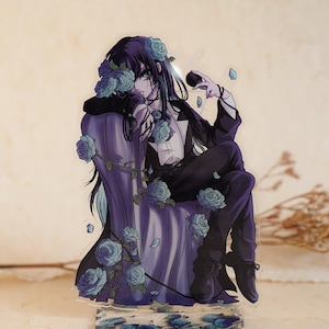 Peut inclure: Un présentoir en acrylique représentant un personnage de style anime aux longs cheveux sombres, vêtu d'un costume noir et d'une chemise blanche, assis sur une chaise drapée de violet. Le personnage est entouré de roses bleu clair et de vignes.