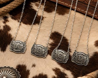 Op de afbeelding: Vier zilverkleurige kettingen met rechthoekige hangers voorzien van ingewikkelde krulgravures. Elke hanger toont een prominente hoofdletter, namelijk A, B, C en D, gecentreerd in het versierde metalen frame aan een fijne ketting.