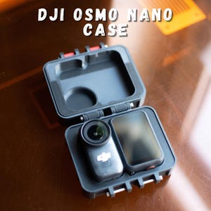 Puede incluir: Estuche negro DJI Osmo Nano abierto, que revela una cámara y una pantalla. El estuche tiene detalles en rojo y el texto blanco "DJI OSMO NANO CASE". La lente de la cámara es visible.