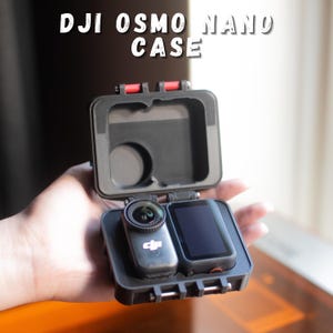 Puede incluir: Estuche negro DJI Osmo Nano abierto, que revela una cámara y una pantalla. La funda tiene detalles en rojo en las bisagras. El texto "DJI OSMO NANO CASE" está impreso en la parte superior de la imagen.