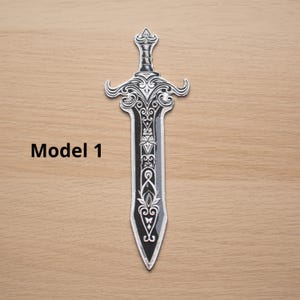 May include: A decorative sword with intricate silver-colored detailing on a black blade. The hilt and blade feature ornate patterns. The text "Model 1" is printed in black on the wooden surface.