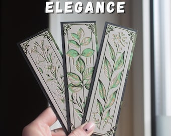 May include: Three rectangular bookmarks with floral designs. The bookmarks have a light gray background with embossed green and gold leaves and flowers. The borders are black. The text "FLORAL ELEGANCE" is at the top.
