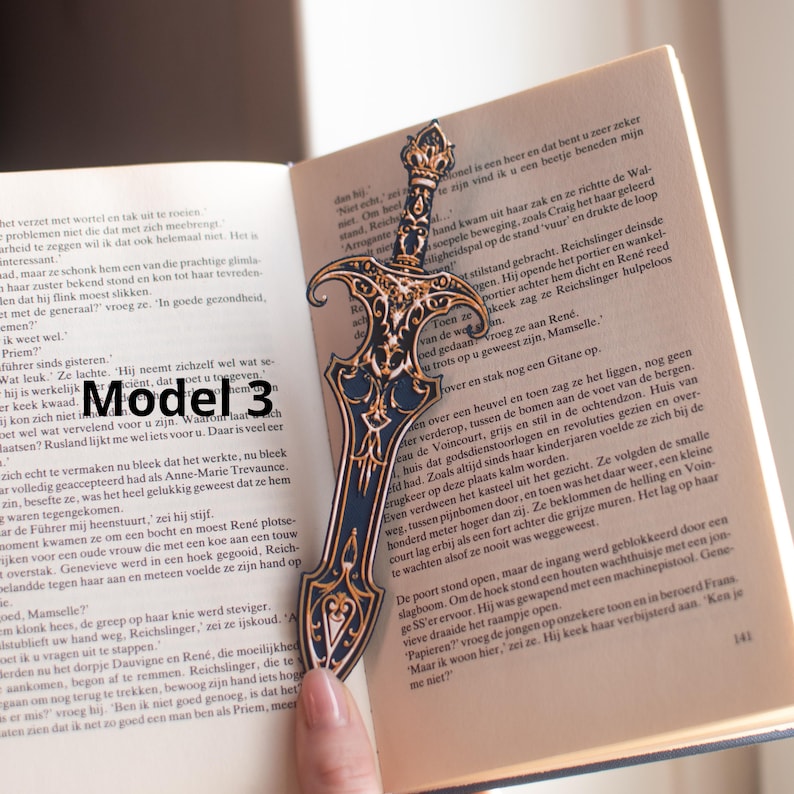 May include: A decorative metal bookmark shaped like a sword, with intricate details and a gold-colored crown. The bookmark is placed in an open book, adding a touch of fantasy to reading.