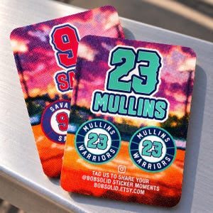 May include: Two rectangular stickers with rounded corners featuring a sunset-colored halftone background. One sticker displays the number 23 and the name MULLINS in teal, with two circular logos reading MULLINS 23 WARRIORS and social media text.