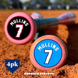 May include: Pink baseball bats with the name "MULLINS" and the number "7" in white. One bat has a black circle, the other has a blue circle. The text "4pk" is in a blue downward-pointing triangle. The website "BOBSOLID.ETSY.COM" is at the bottom.