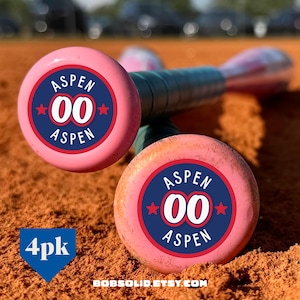 May include: Two pink baseball bats featuring a circular navy blue logo on the end cap. The logo displays the text ASPEN in white, the number 00 in white, and two red stars. A blue shield graphic in the corner contains the white text 4pk.