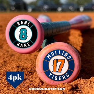May include: Pink baseball bats with custom designs. One bat features "KANE 8 KANE" in a teal and black circle, the other says "MULLINS 17 TIGERS" in orange and blue. The bats are on a brown surface. The text "4pk" and "BOBSOLID.ETSY.COM" are also visible.