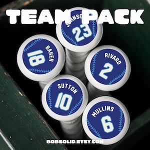 May include: Five white baseball bat knobs featuring circular blue decals with baseball stitching graphics. Each decal displays a player name and jersey number: Baker 18, Johnson 23, Rivard 2, Sutton 10, and Mullins 6. The text TEAM PACK is at the top.