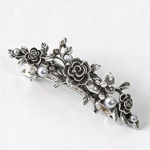 May include: Silver-toned metal hair clip featuring a floral design with roses, leaves, and faux pearls. The barrette has a decorative arrangement of flowers and pearl accents, suitable for various hairstyles.