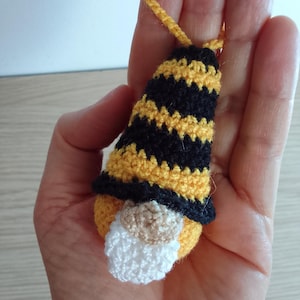 May include: A small crocheted gnome ornament with a black and yellow striped hat. The gnome has a white beard and a brown face.
