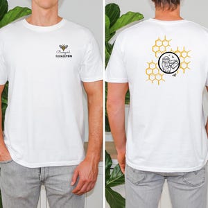 May include: White t-shirt with a bee and the words "Backyard Beekeeping" on the front. The back of the shirt features a honeycomb design with a beekeeper illustration. The shirt is made of a soft material and is suitable for casual wear.