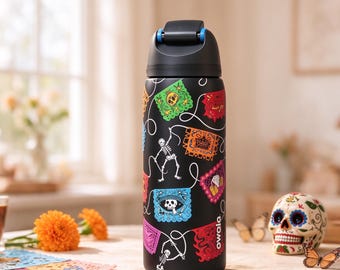 May include: A black water bottle featuring a colorful pattern of papel picado banners and skeletons. The bottle has a black lid with a blue accent and the brand name Owala printed in white near the base. The design includes various bright colors.