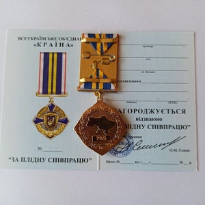 May include: A Ukrainian medal and certificate. The medal is gold-colored with a map of Ukraine and the number 755. The certificate has text in Ukrainian. The medal has blue and yellow ribbons.