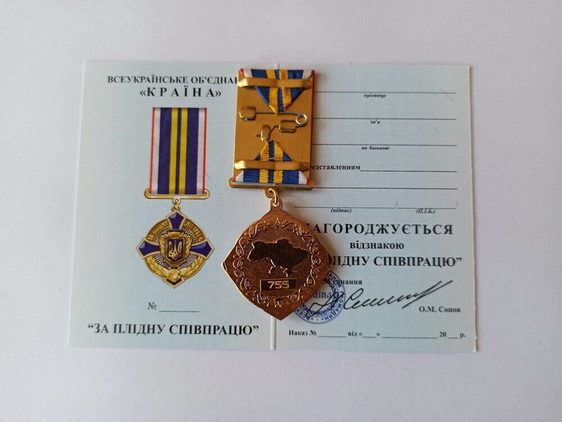 May include: A Ukrainian medal and certificate. The medal is gold-colored with a map of Ukraine and the number 755. The certificate has text in Ukrainian. The medal has blue and yellow ribbons.