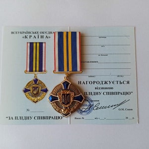 May include: A Ukrainian medal with a blue and yellow striped ribbon, a gold-colored cross-shaped emblem, and the text "ЗА ПЛІДНУ СПІВПРАЦЮ" on a certificate. The medal features a blue and gold emblem.