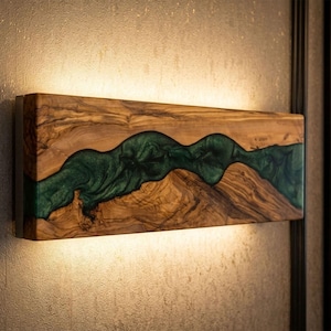 May include: A rectangular wall-mounted light fitting featuring a natural wood grain body with a central, flowing inlay of translucent emerald green resin. The fitting emits a soft, warm glow from both the top and bottom edges.