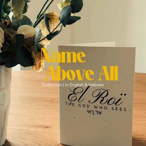 Peut inclure: Carte de vœux avec le texte "Name Above All" et "El Roi, The God Who Sees" en anglais et en hébreu. La carte est posée sur une surface en bois, avec un vase de fleurs en arrière-plan.