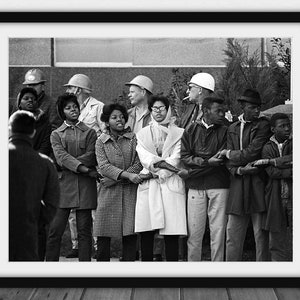 May include: Black and white framed photograph of a group of people, some wearing coats and hats, standing close together and holding hands. The photograph appears to be from the civil rights era.