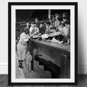 Könnte beinhalten: Schwarz-Weiß-Druck in einem Rahmen, der einen Baseballspieler zeigt, der Autogramme für eine Menge von Fans gibt. Der Spieler trägt eine Baseballuniform und eine Kappe. Ein kleiner Junge steht daneben und beobachtet. Vintage-Fotografie.