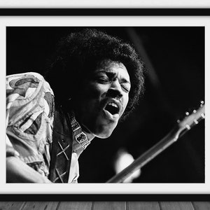May include: Monochrome framed print featuring a musician mid-performance, singing and playing a guitar. The musician is wearing a patterned shirt and a necklace. The image is a close-up, highlighting the musician's expression and guitar details.