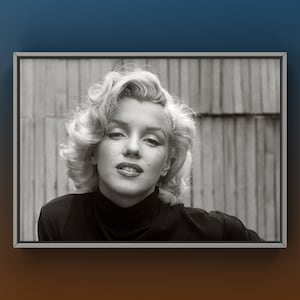 Puede incluir: Retrato enmarcado en blanco y negro de Marilyn Monroe. La imagen muestra un primer plano de la actriz con sus característicos rizos rubios, delineador de ojos oscuro y un cuello alto negro. El fondo es una pared de madera.