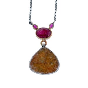May include: A necklace featuring a dark metal chain attached to a central oval-shaped deep pink gemstone, flanked by two smaller marquise-cut pink stones, with a large, textured, pear-shaped amber-colored stone pendant suspended below.