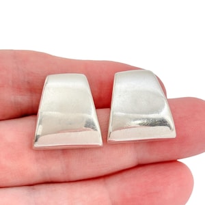May include: A pair of silver-toned, geometric earrings. Each earring has a rectangular base that tapers upwards, with a slightly curved top. The earrings are smooth and reflective, with a polished finish.