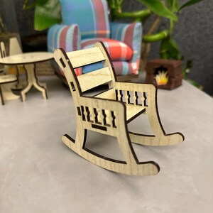 May include: A wooden rocking chair with a slatted back and a carved design on the arms and rockers. The chair is light brown and has a natural wood finish.
