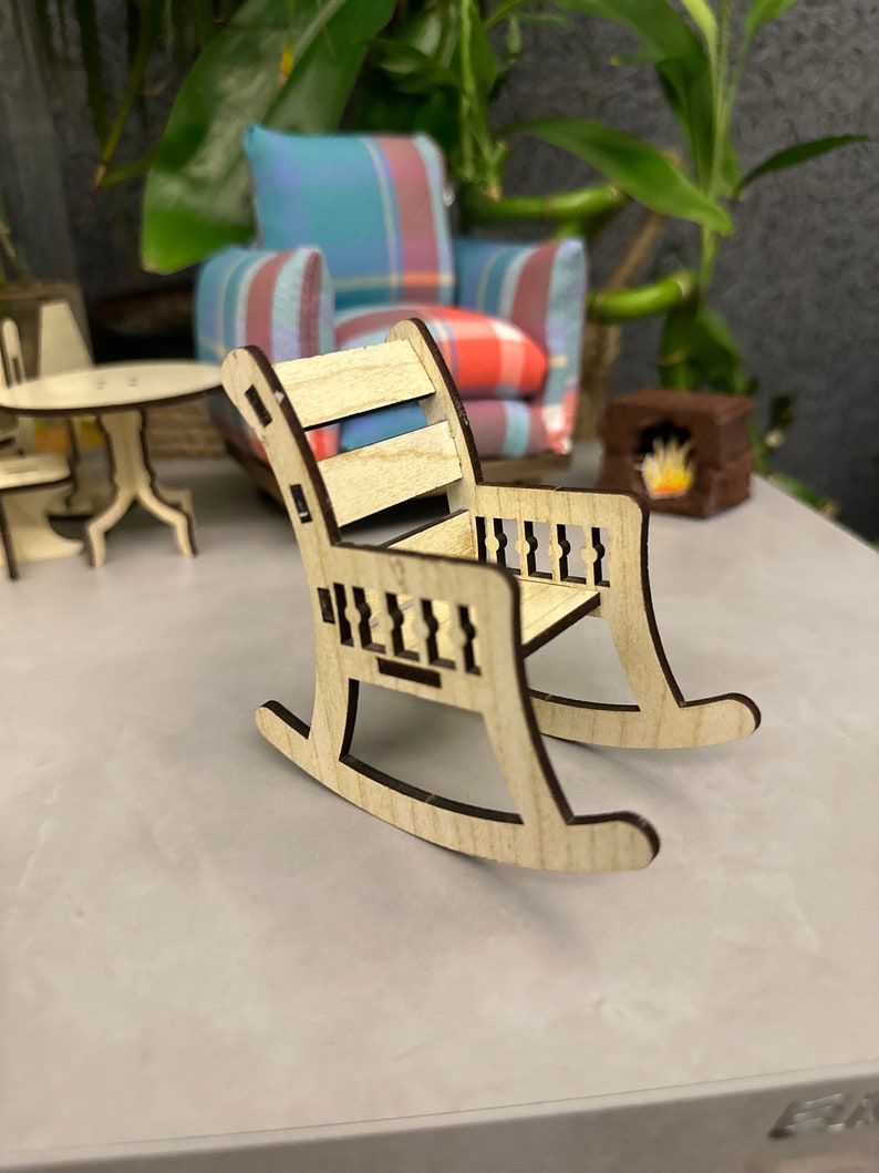 May include: A wooden rocking chair with a slatted back and a carved design on the arms and rockers. The chair is light brown and has a natural wood finish.