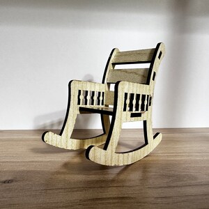 May include: A small wooden rocking chair with a black outline. The chair has a slatted back and a simple design.