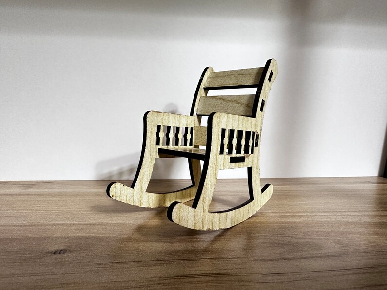 May include: A small wooden rocking chair with a black outline. The chair has a slatted back and a simple design.