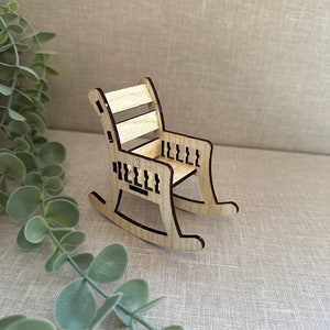 May include: A miniature wooden rocking chair with a brown stain. The chair has a slatted back and a carved design on the arms and rockers.