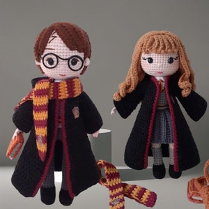 Könnte beinhalten: Zwei gehäkelte Puppen, die als Harry Potter und Hermine Granger verkleidet sind. Die Puppen tragen schwarze Roben mit roten Akzenten und Gryffindor-Schals. Die Puppen haben braunes bzw. blondes Haar.