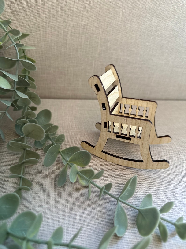 May include: A miniature wooden rocking chair with a light brown finish. The chair has a slatted back and a simple design.