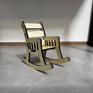 May include: A wooden rocking chair with a natural wood finish and black accents. The chair has a simple design with a curved back and a wide seat.