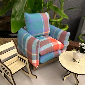 May include: A miniature living room set with a plaid armchair, a rocking chair, and a small wooden table. The set is made of wood and fabric and is painted in natural wood tones and a blue and red plaid pattern.