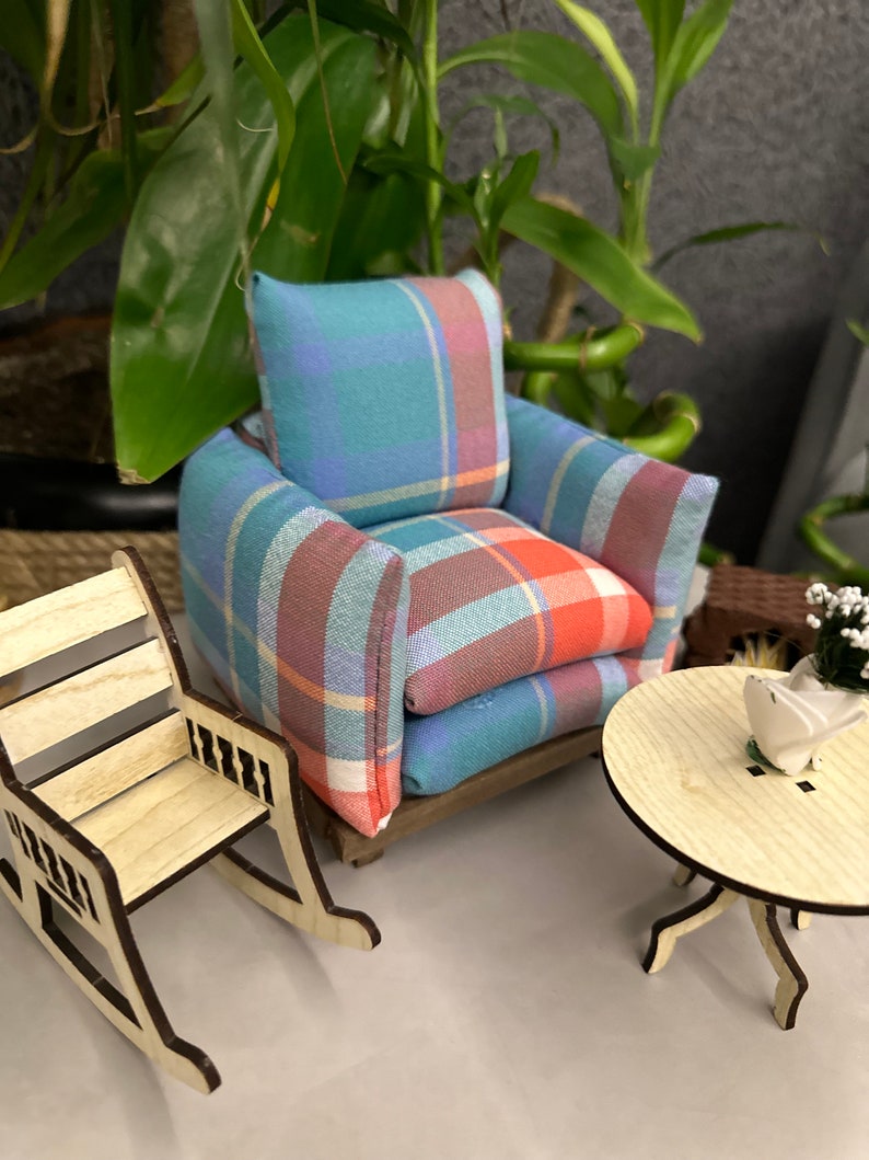 May include: A miniature living room set with a plaid armchair, a rocking chair, and a small wooden table. The set is made of wood and fabric and is painted in natural wood tones and a blue and red plaid pattern.