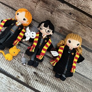 May include: Three crocheted Harry Potter characters, including Harry Potter, Ron Weasley, and Hermione Granger, with their respective animal companions: Hedwig the owl, Scabbers the rat, and Crookshanks the cat. The characters are wearing black robes with Gryffindor house scarves.