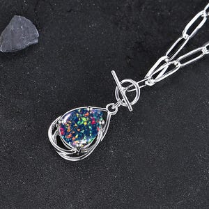 May include: A silver chain necklace with a silver toggle clasp and a teardrop-shaped pendant featuring a black opal gemstone.