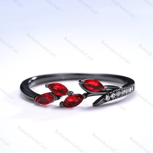 May include: Black ring with a delicate branch design featuring red marquise-shaped gemstones and small clear round stones.