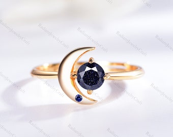 May include: Gold ring with a crescent moon design and a blue gemstone. The ring features a smaller blue gemstone on the moon.