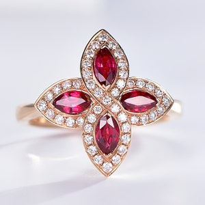 May include: A gold ring with a four-leaf clover design featuring red ruby gemstones and smaller white diamonds.