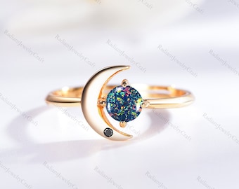 May include: A gold ring with a crescent moon design and a round, iridescent opal gemstone. A small black diamond is set on the moon.