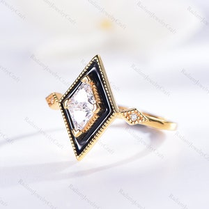 Op de afbeelding: Een gouden ring met een zwarte emaille setting en een vierkante, heldere edelsteen. De ring heeft een delicaat ontwerp met kleine diamanten op de band.