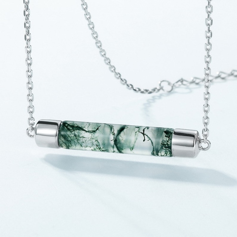 May include: A silver chain necklace with a green moss agate pendant. The pendant is a long, thin cylinder with a silver cap on each end.
