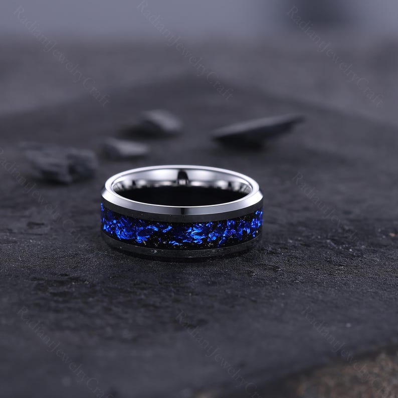 Peut inclure: Une bague argent&eacute;e avec une bande int&eacute;rieure noire et une incrustation bleue vibrante. L'incrustation bleue a un aspect textur&eacute; et cristallin. La bague est pos&eacute;e sur un fond sombre et textur&eacute;.