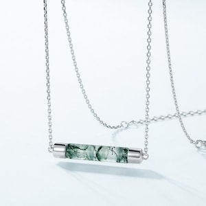 May include: A silver chain necklace with a green moss agate bar pendant. The pendant is a clear, translucent bar with green moss agate inclusions.