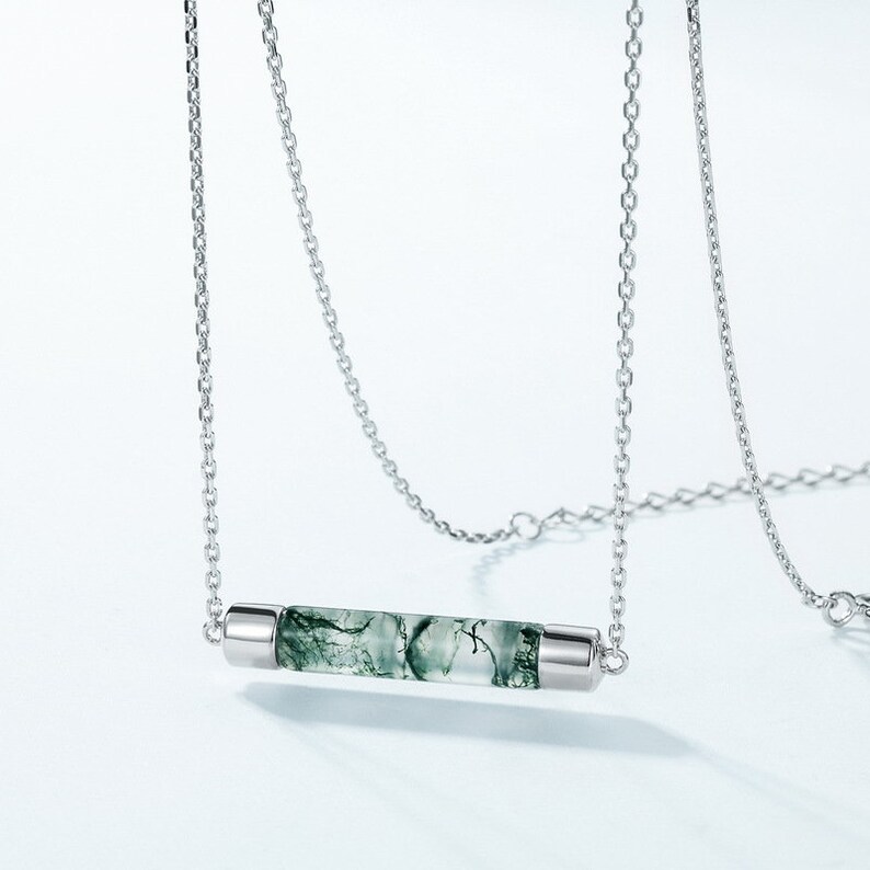 May include: A silver chain necklace with a green moss agate bar pendant. The pendant is a clear, translucent bar with green moss agate inclusions.