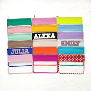 Puede incluir: Una colección de 14 bolsas transparentes con cremallera y diferentes frentes de tela de colores. Las bolsas tienen diferentes nombres en la parte delantera, incluyendo "Alexa", "Emily" y "Julia".