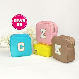 May include: Four small zippered pouches in different colors with a large white letter sewn on the front. The pouches are pink, blue, brown, and yellow. The letters are Z, C, K, and a blank yellow pouch.